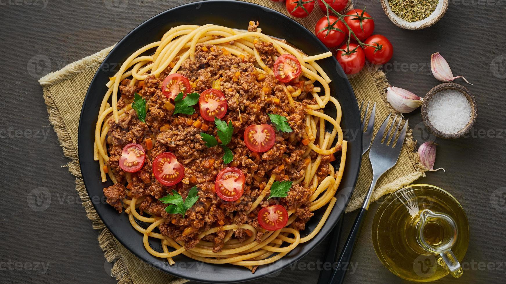 bucatini di pasta alla bolognese con carne macinata e pomodori, fondo in legno scuro, vista dall'alto, striscione lungo foto