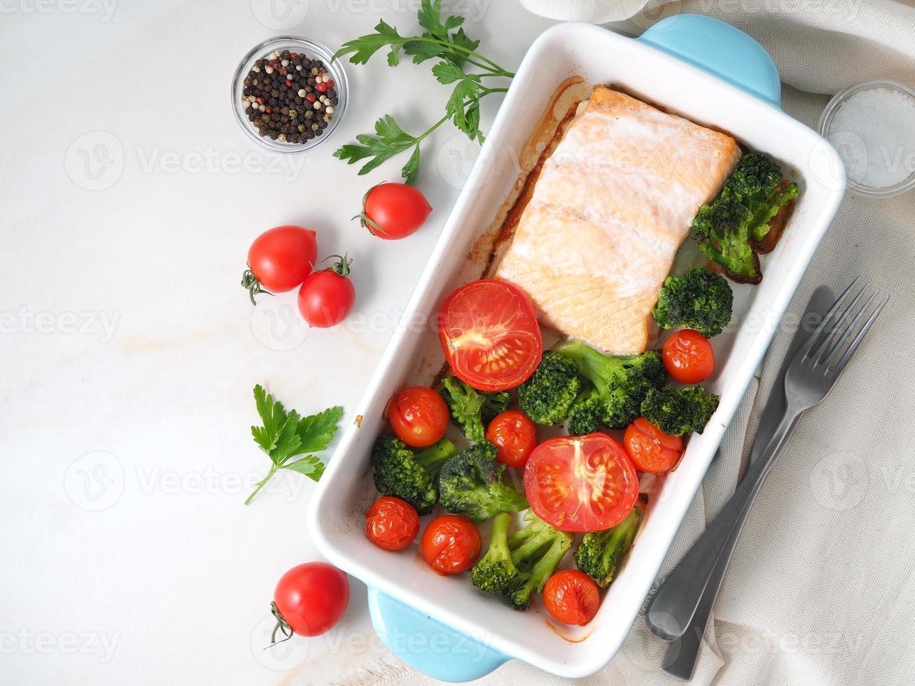 salmone di pesce al forno con verdure - broccoli, pomodori. cibo dietetico sano, marmo bianco foto