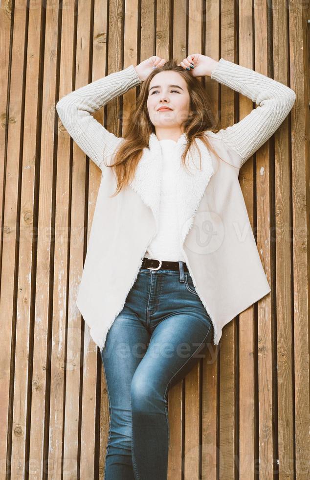 Ritratto di bella ragazza con lunghi capelli castani sdraiato e rilassante su sfondo di legno di assi, inverno o autunno servizio fotografico all'aperto con donna attraente foto