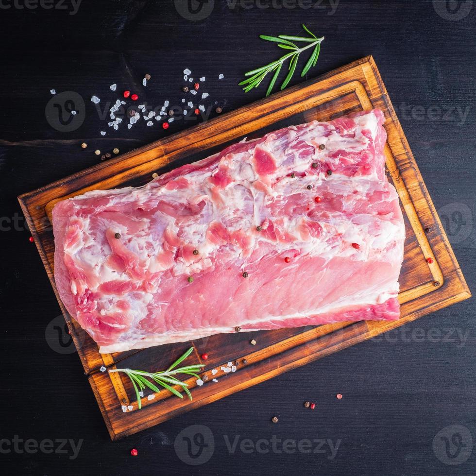 grande pezzo intero di carne di maiale con condimento sul tagliere su fondo scuro foto