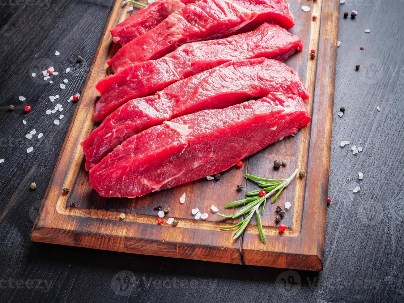 carne cruda, bistecca di manzo con condimento su tagliere su fondo scuro al rosmarino, foto