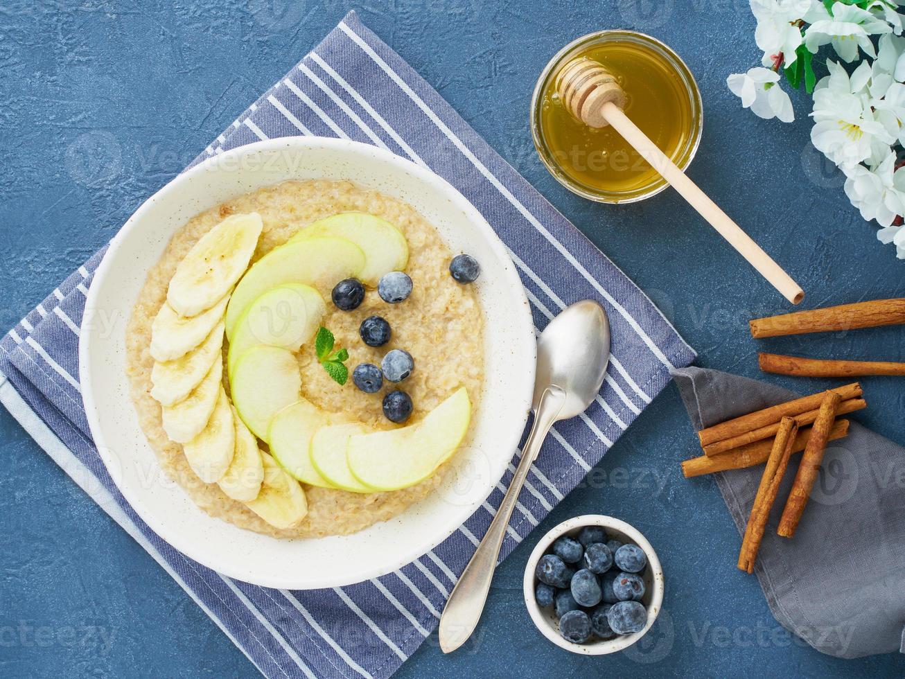 farina d'avena con banane, mirtilli, marmellata, miele, tovagliolo blu su sfondo di pietra blu. foto