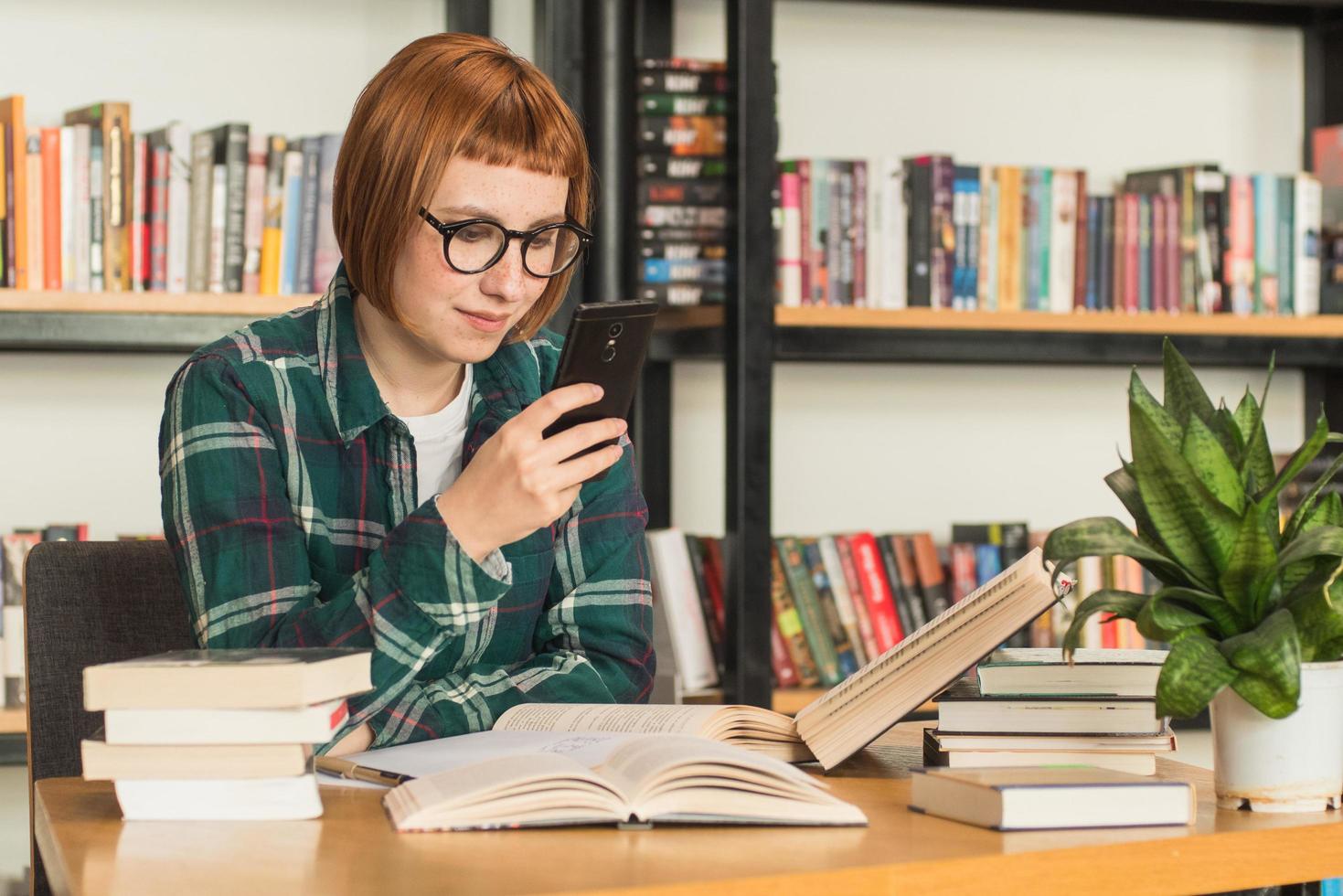 giovane donna rossa con gli occhiali legge il libro in biblioteca foto