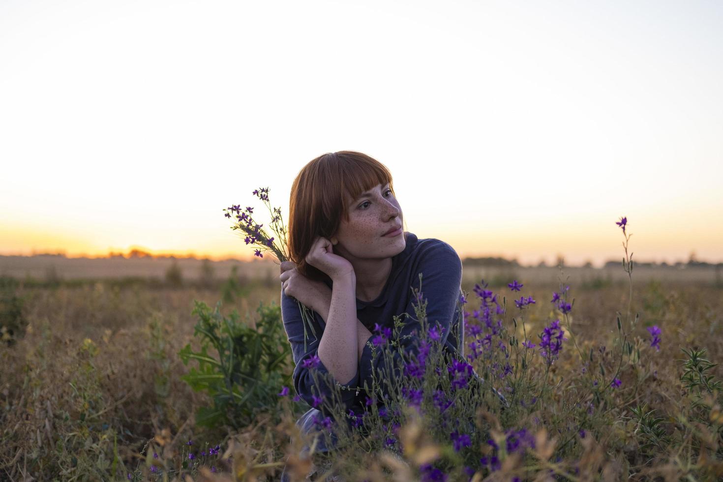 giovane donna rossa con le lentiggini in abito vintage fatto a mano cammina nei campi con fiori foto