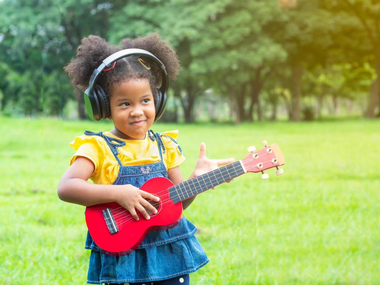 la ragazza sta sull'erba, indossa le cuffie e sta imparando a suonare le corde dell'ukulele foto