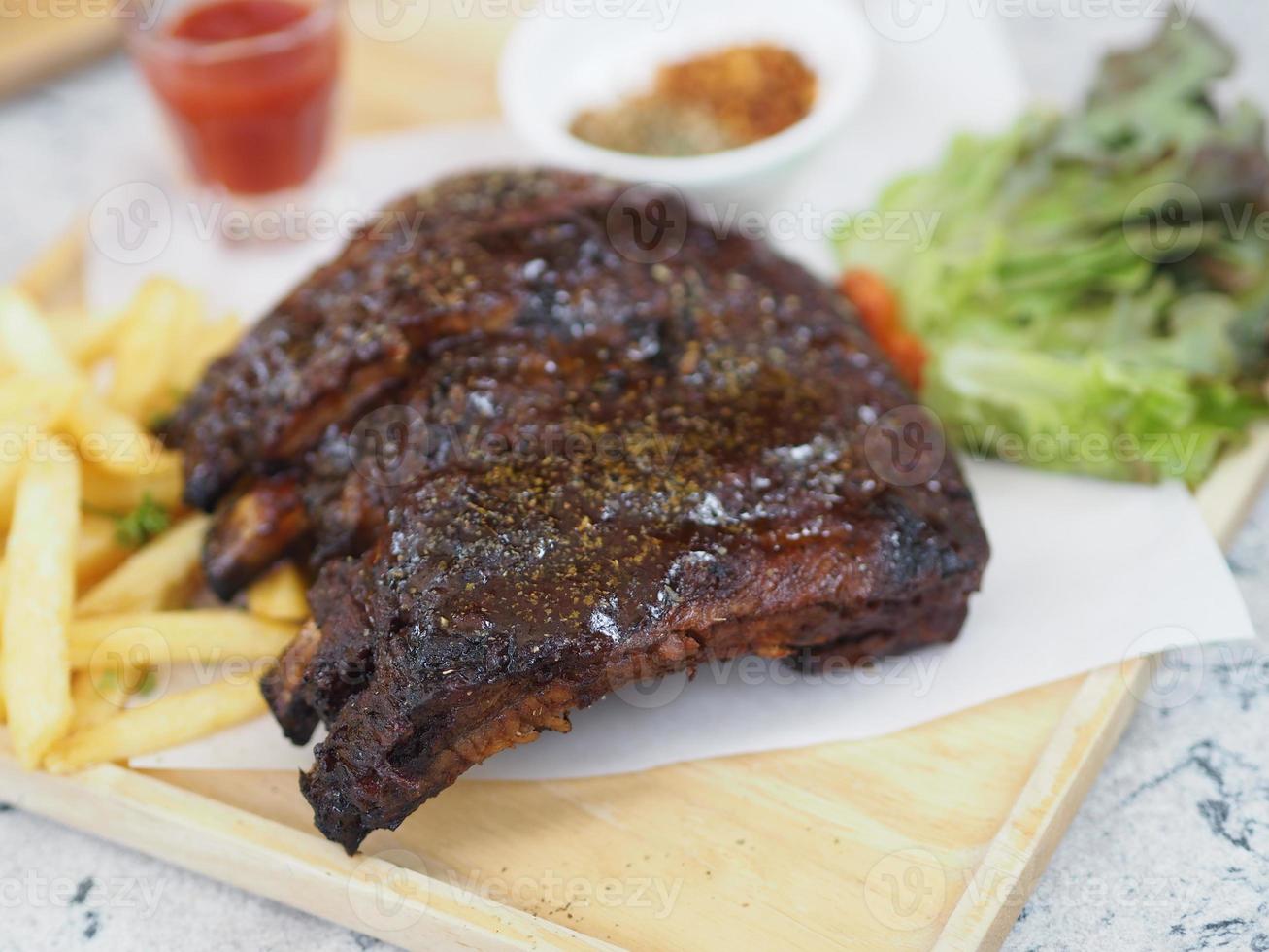 costolette di maiale barbecue, barbecue costolette di maiale con patatine fritte insalata di verdure, salsa di pomodoro in un bicchiere trasparente su vassoio di legno, cibo foto