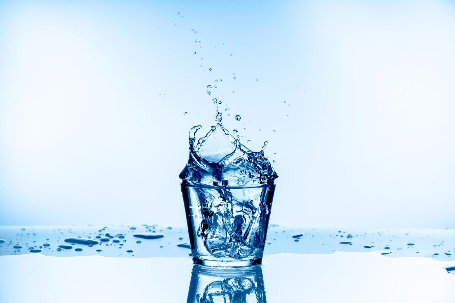 ghiaccio caduto nel bicchiere con spruzzi d'acqua dal vetro isolato su sfondo blu foto