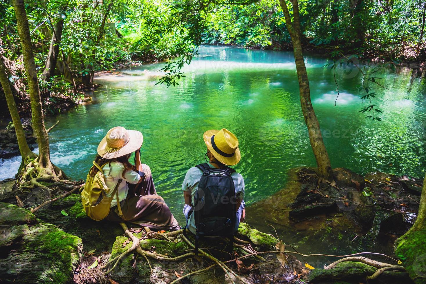 i viaggiatori si accoppiano con gli zaini seduti e si rilassano sugli scogli. viaggiare nella natura nella giungla verde e godersi la vista nella cascata. turismo, escursionismo, studio della natura. coppie che viaggiano per scattare foto