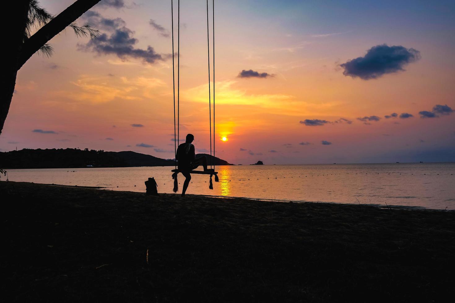 la gente della siluetta si siede sull'altalena con il bel cielo della nuvola del tramonto sull'oceano idilliaco foto