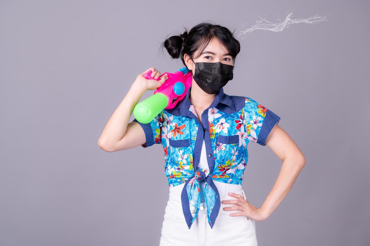 le belle donne asiatiche indossano una maschera chirurgica mentre tengono una pistola ad acqua di plastica durante il festival di Songkran foto