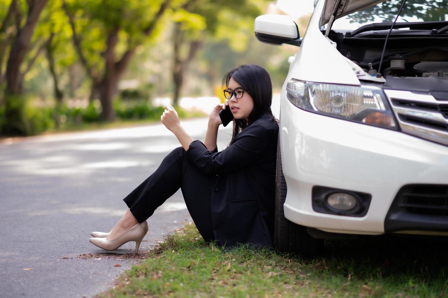 una giovane donna asiatica sta chiamando il suo tecnico dell'assistenza per riparare un'auto rotta sul ciglio della strada foto