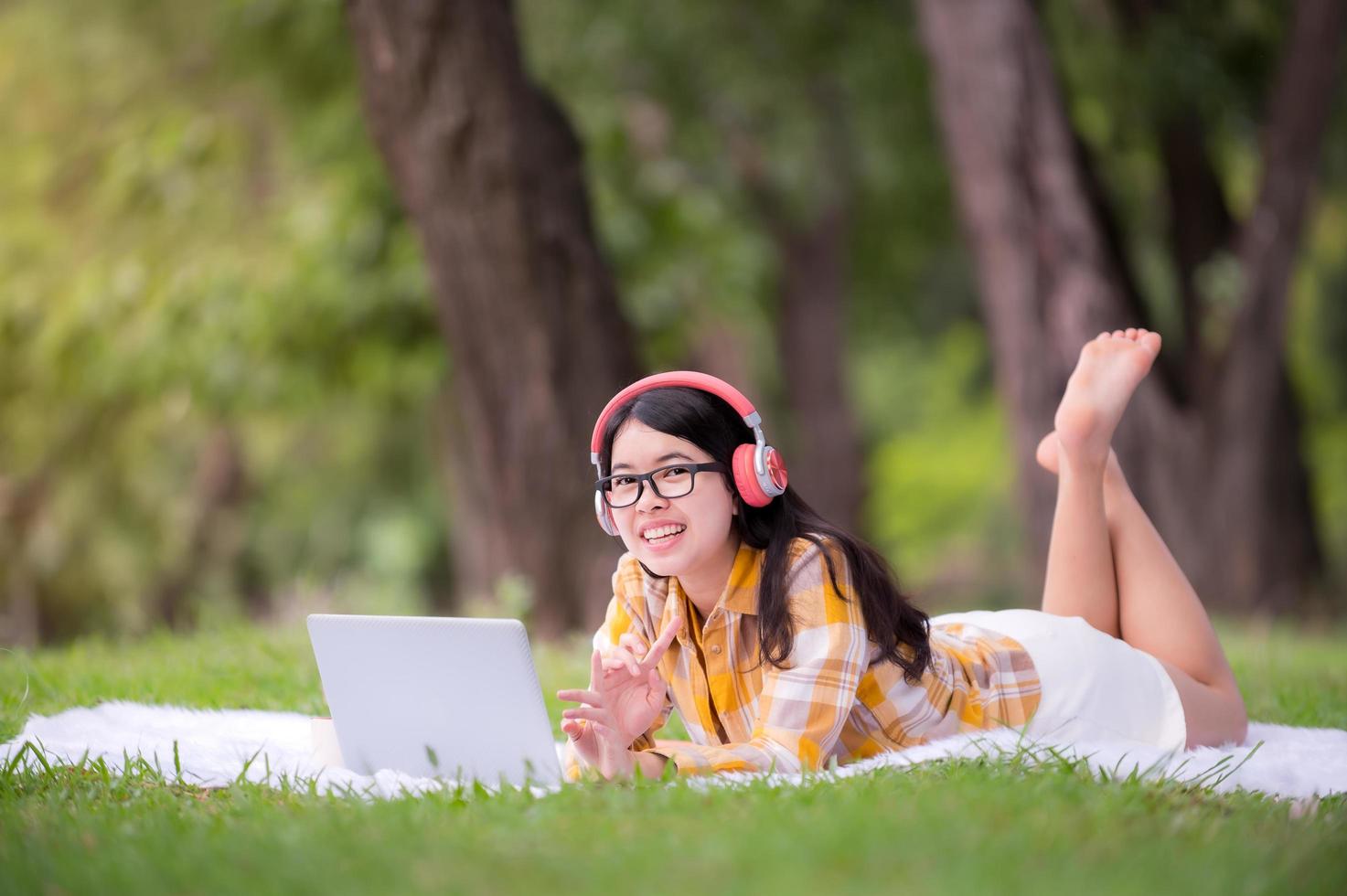 una bella donna asiatica si sta rilassando in giardino, legge e cerca informazioni di apprendimento da Internet foto