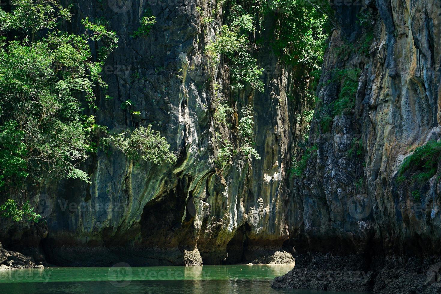 montagna rocciosa con gli alberi crescono sulla scogliera con il lago sottostante nella giornata di sole foto