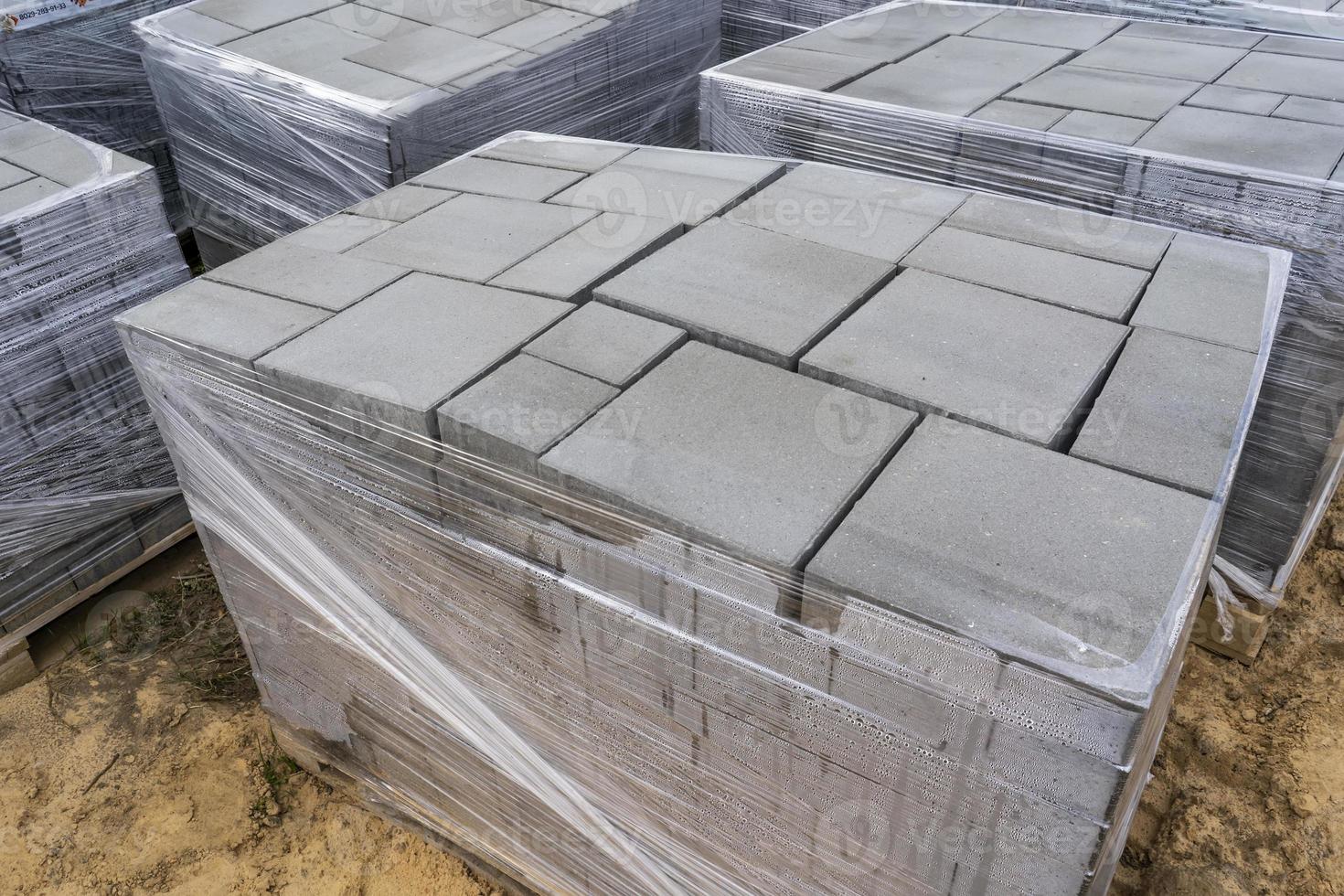 posa di lastre di pavimentazione in cemento grigio nel patio carraio del cortile della casa. muratori professionisti installano nuove piastrelle o lastre per il vialetto, il marciapiede o il patio su una base sabbiosa piatta. foto