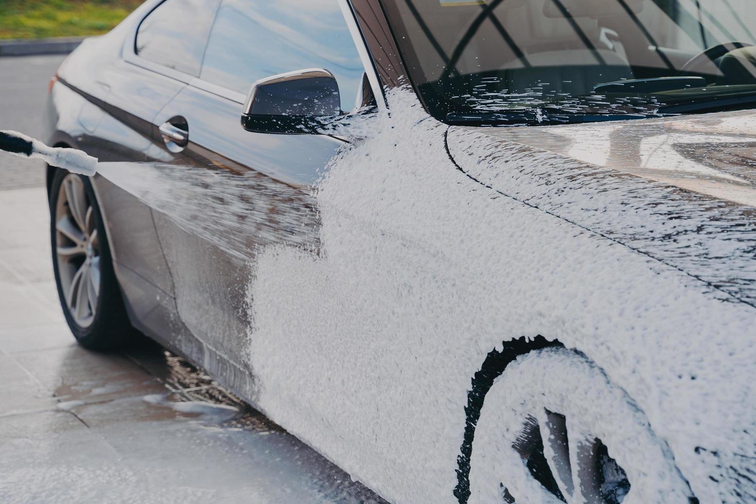 pulizia dell'auto ad alta pressione, spruzzando sapone speciale sul veicolo con idropulitrice all'aperto foto