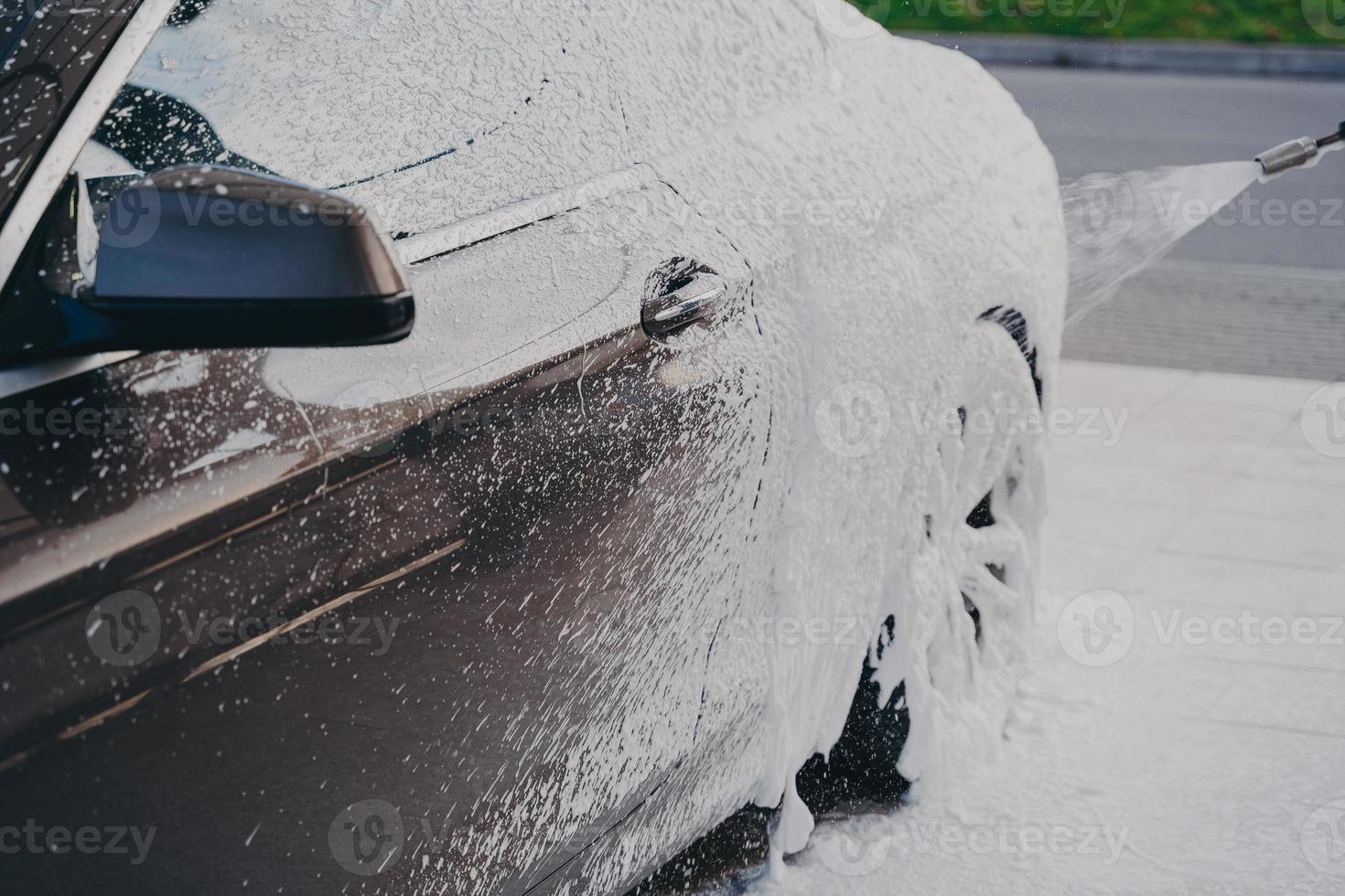 auto di lusso nera in schiuma di neve bianca durante l'autolavaggio all'aperto foto