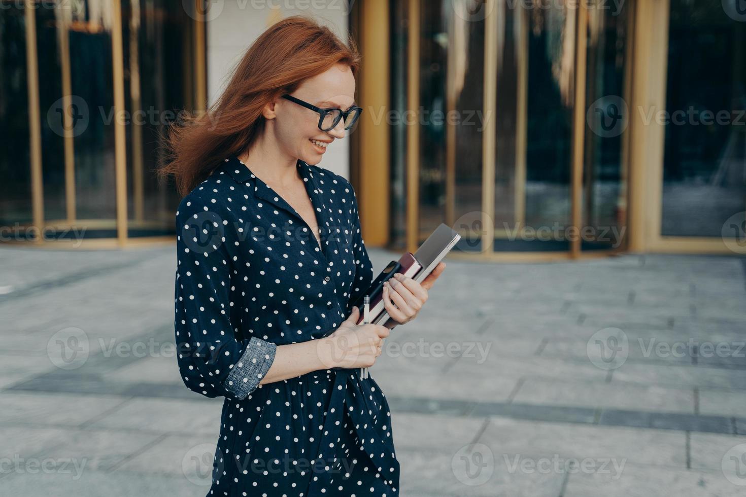 l'operaia esecutiva femminile passeggiate all'aperto guarda in basso indossa felicemente occhiali vestito a pois foto