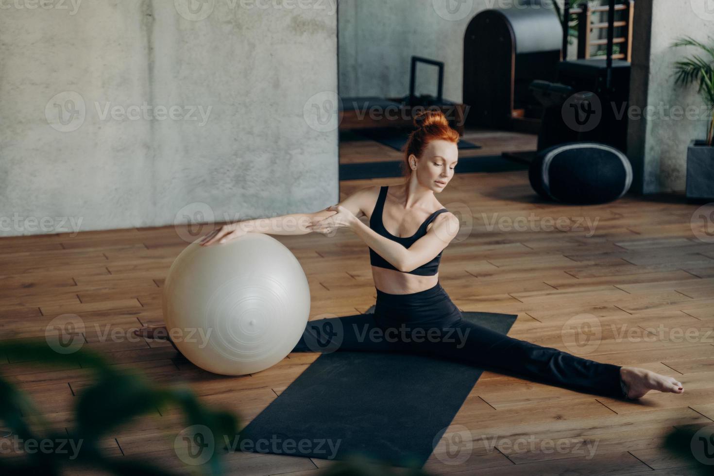 giovane donna in posizione divisa che si esercita con fitball in palestra foto