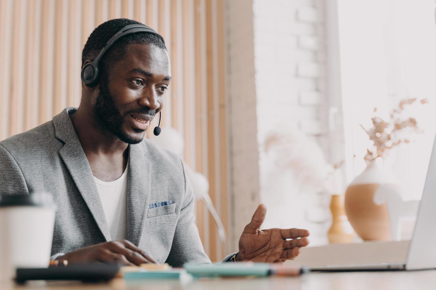giovane uomo afroamericano sorridente in cuffia che consulta il cliente del cliente tramite videochiamata sul laptop foto
