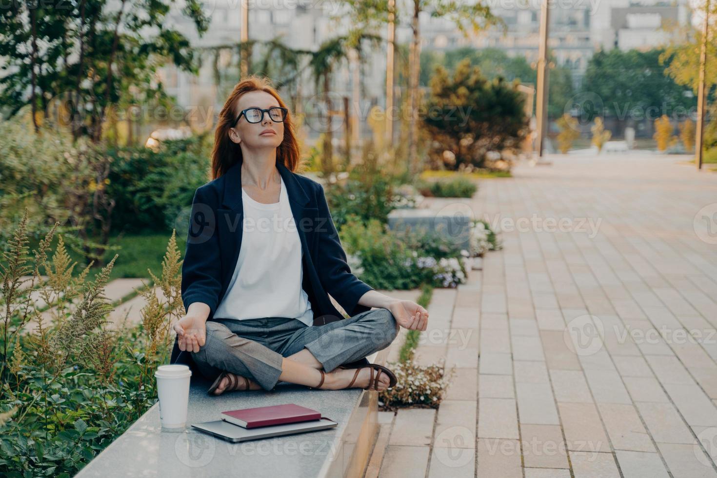 calma donna d'affari che medita nel loto all'aperto, pacifica dipendente freelance femminile che pratica yoga foto