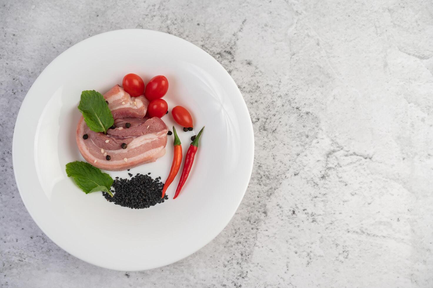 piatto bianco di maiale con semi di pepe e pomodori. foto