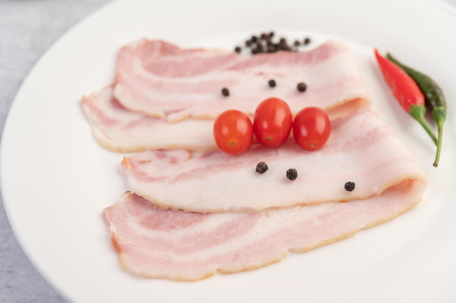 pancetta di maiale un piatto bianco con semi di pepe e pomodori. foto