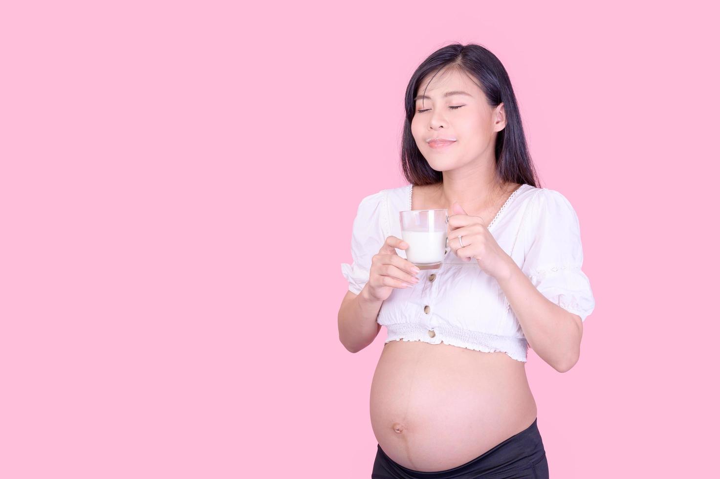 una bella donna incinta in piedi e che beve latte fresco per una buona salute per il suo futuro bambino foto