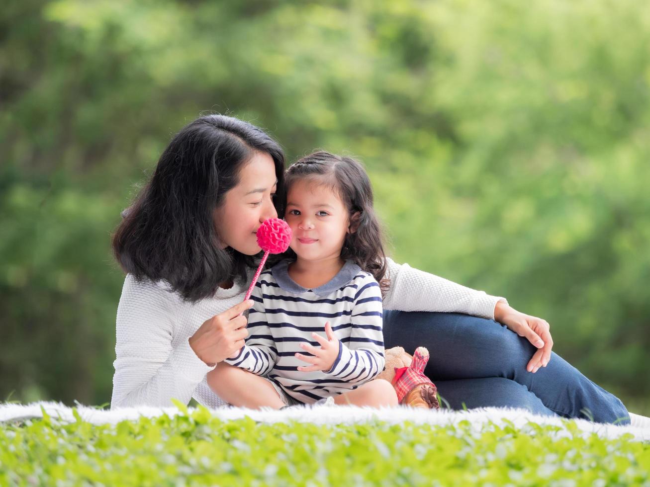 bambina asiatica seduta con sua madre sul panno, rilassarsi e imparare fuori dalla scuola per divertirsi nel parco naturale foto