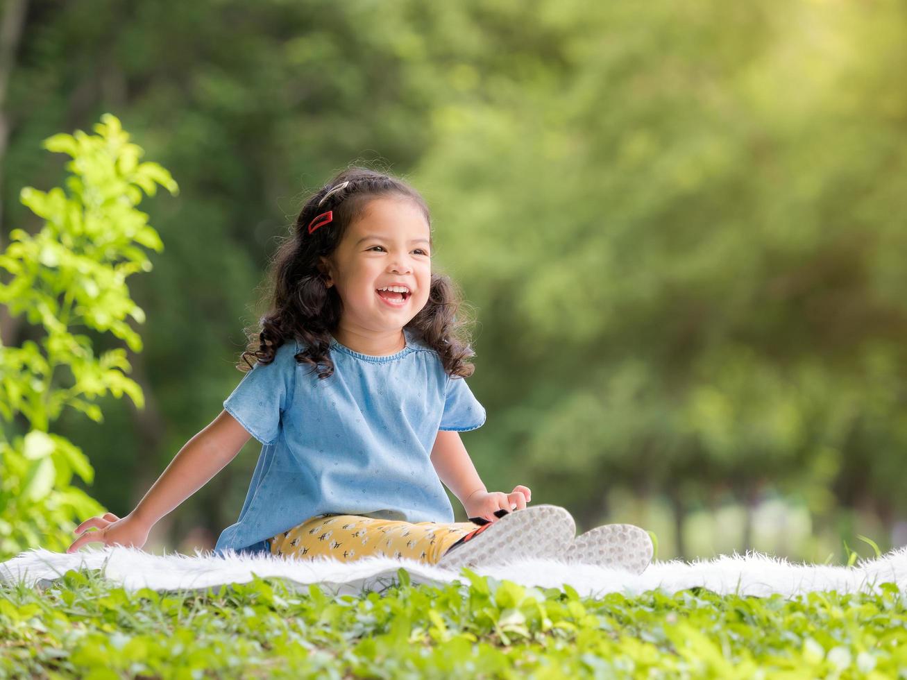 bambina asiatica seduta sul tappeto, rilassarsi e imparare fuori dalla scuola per divertirsi nel parco naturale foto