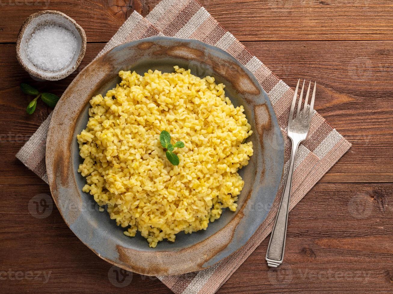 grano bulgur. cereali bulghur bolliti in piatto su tavola di legno marrone. vegetariano sano foto