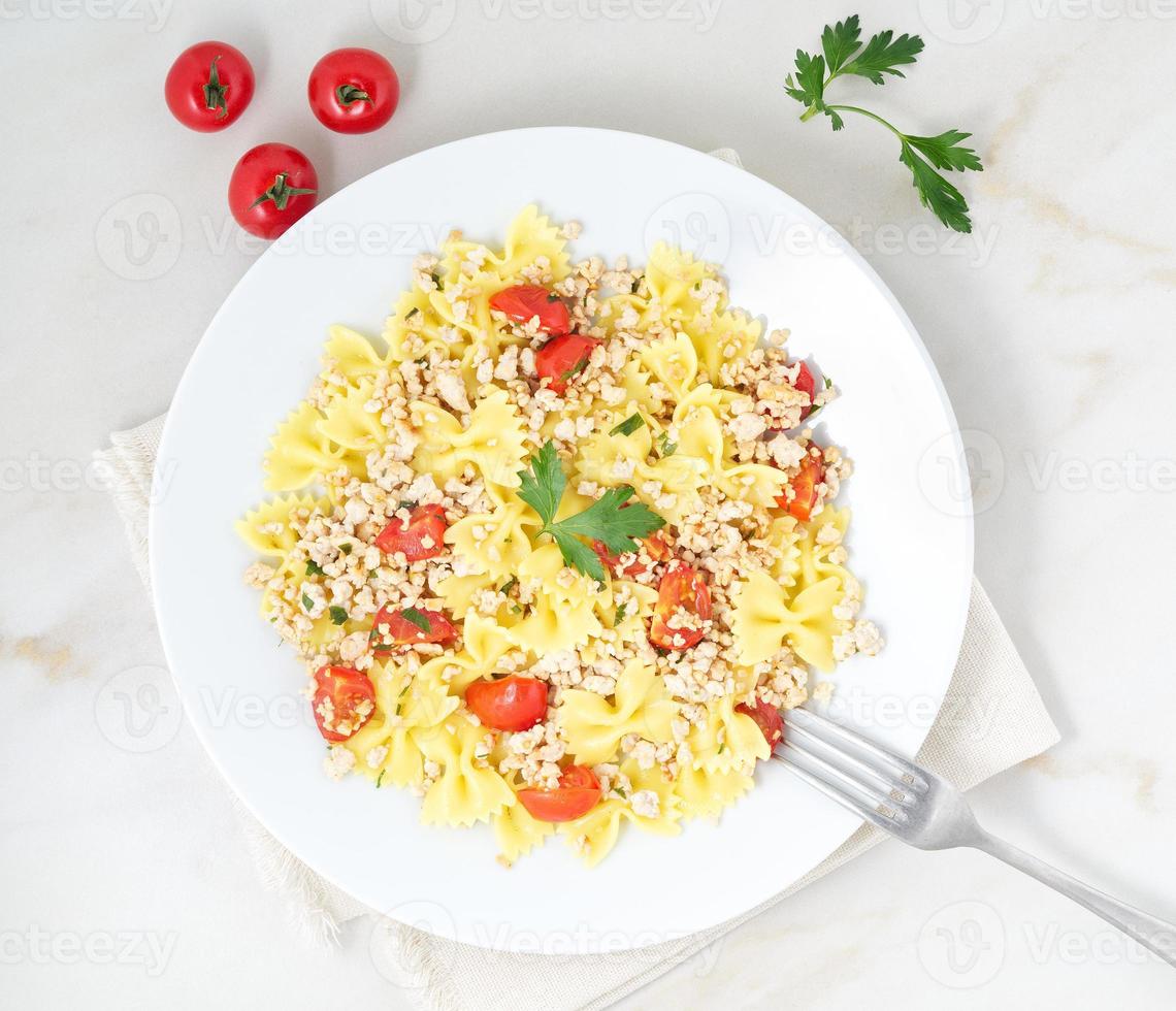 Farfalle con pomodori, carne di pollo, prezzemolo su fondo di pietra bianca, dieta ipocalorica, vista dall'alto foto