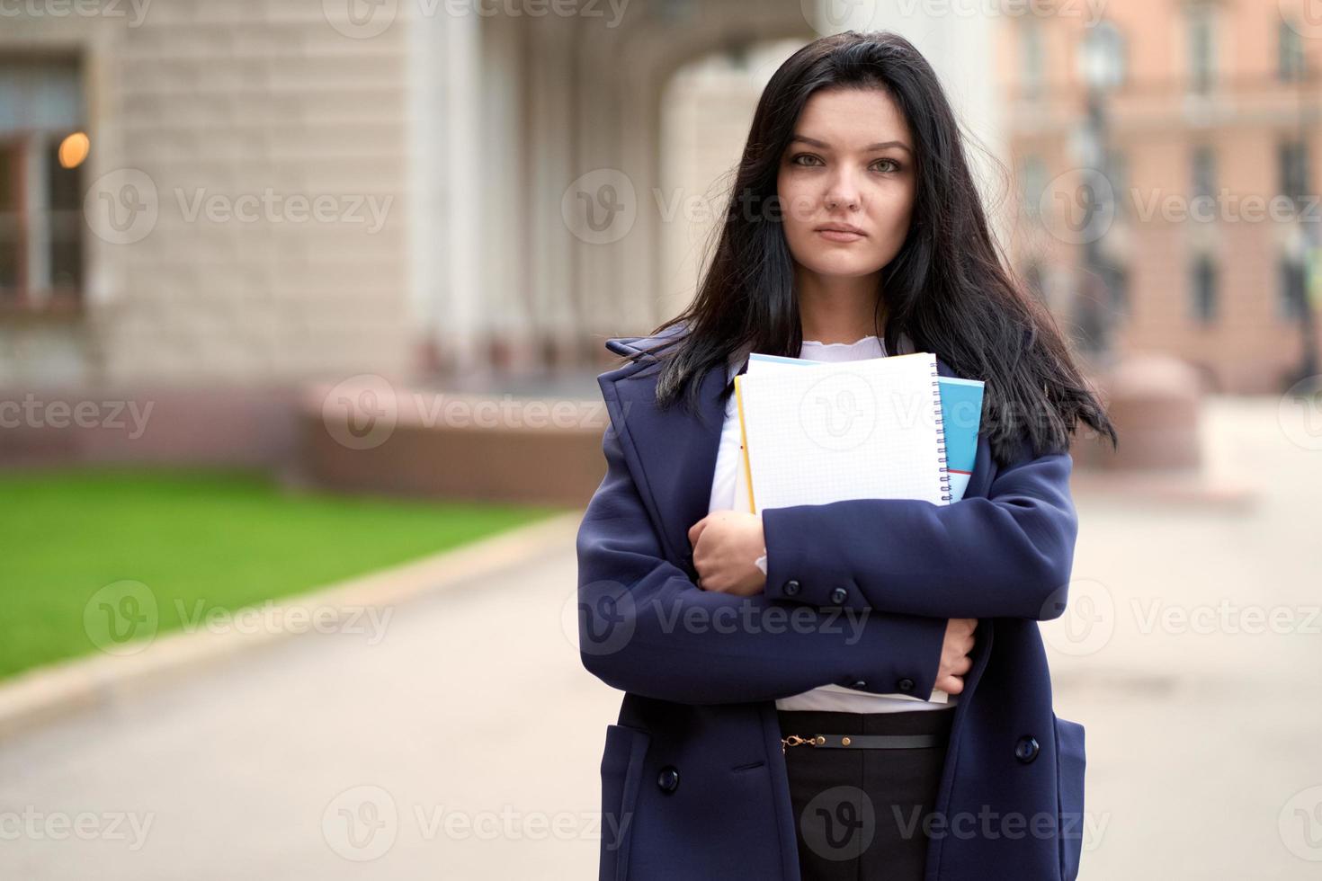 bella ragazza bruna seria intelligente che tiene quaderni e libri di testo, si trova all'università sulla strada di st. pietroburgo. una donna affascinante con lunghi capelli scuri sta studiando al corso foto