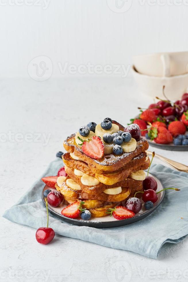 toast alla francese con frutti di bosco e banana, colazione con brioche, primo piano verticale su sfondo bianco foto