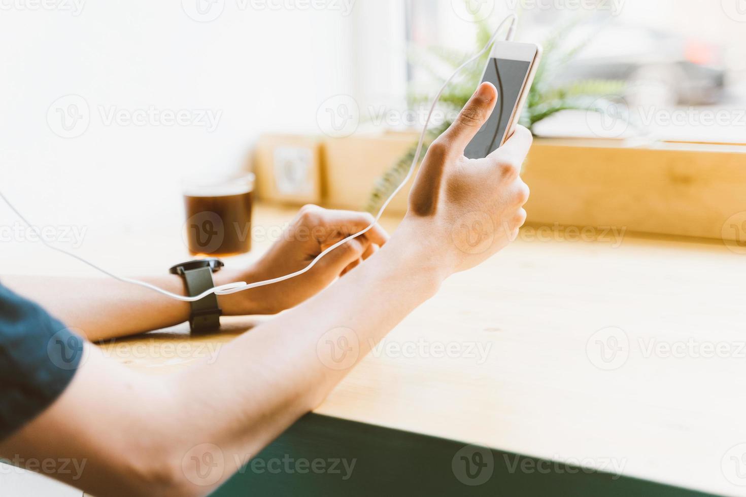 giovane adulto ragazzo, uomo, persona irriconoscibile messaggio di testo sullo smartphone e ascoltare musica con le cuffie nella caffetteria. stile di vita, tempo libero, riposo, relax foto