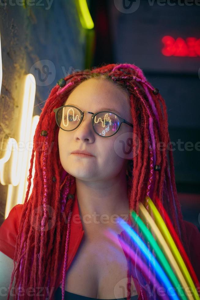 ragazza con luci al neon, bella donna con occhiali da sole, con i capelli rosa, con le trecce dreadlocks foto