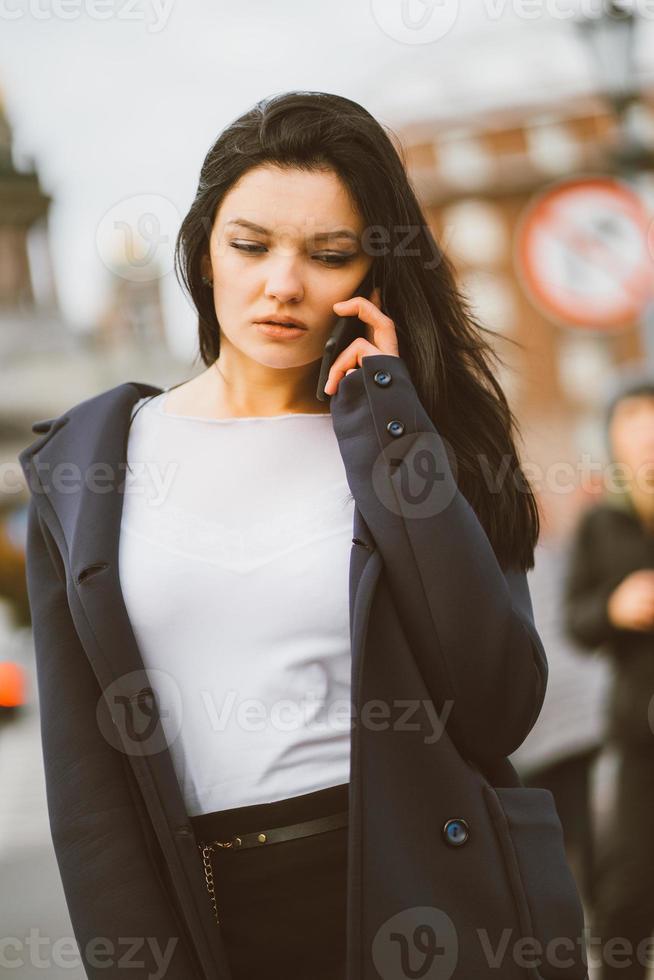 donna con i capelli lunghi che parla al telefono. autunno o inverno, ragazza all'aperto. bella bruna intelligente in strada di san pietroburgo nel centro della città, copia spazio foto