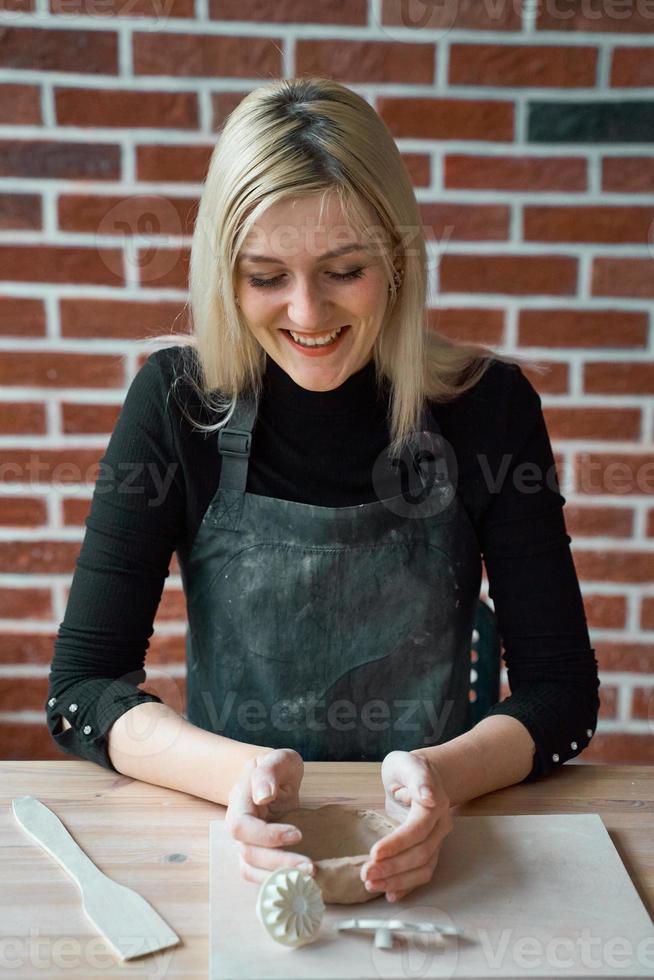 donna sorridente felice che fa ceramica, rubinetto con spatola. concetto per donna in freelance, affari. prodotto artigianale. guadagnare soldi extra, fare affari, trasformare gli hobby in denaro, la passione in lavoro foto