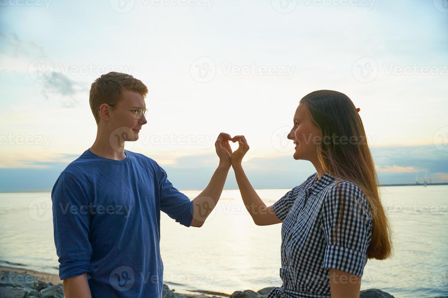 storia d'amore di due, ragazzo e ragazza che fanno il cuore con le dita, sfondo spiaggia foto