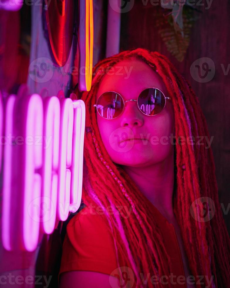 ragazza con luci al neon, bella donna con occhiali da sole, con i capelli rosa, con le trecce dreadlocks foto