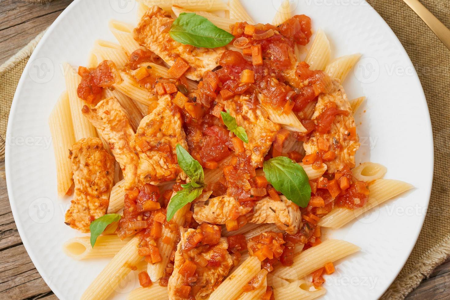 penne, filetto di pollo o tacchino, salsa di pomodoro con foglie di basilico su vecchio fondo di legno rustico. vista dall'alto, primo piano foto