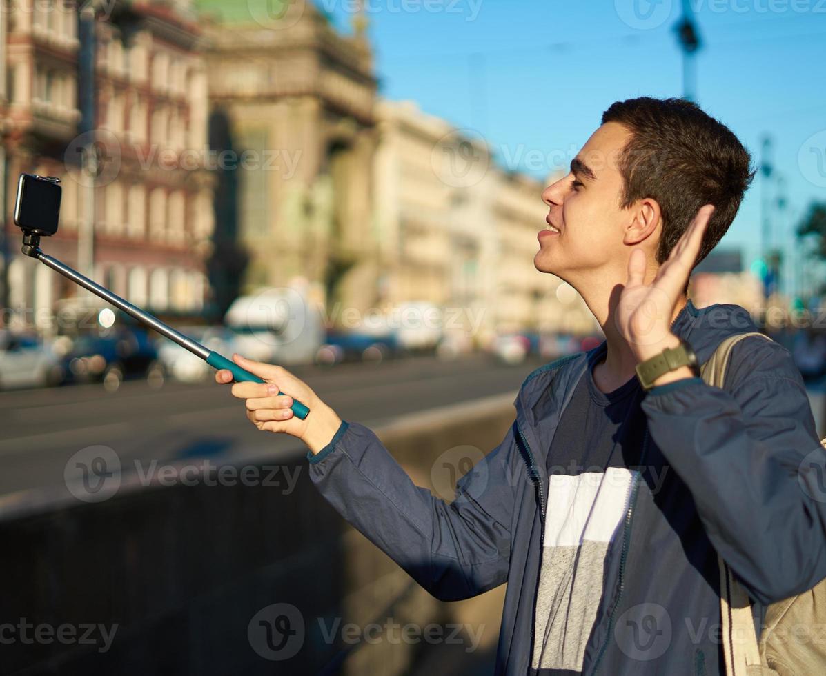 il giovane con un telefono è sulla strada di una grande città e agita la mano foto