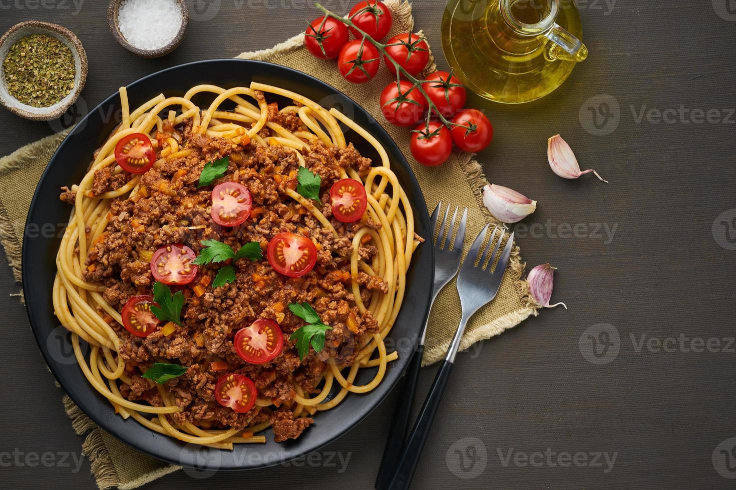 bucatini di pasta alla bolognese con carne macinata e pomodori, fondo in legno scuro, vista dall'alto, spazio per la copia foto