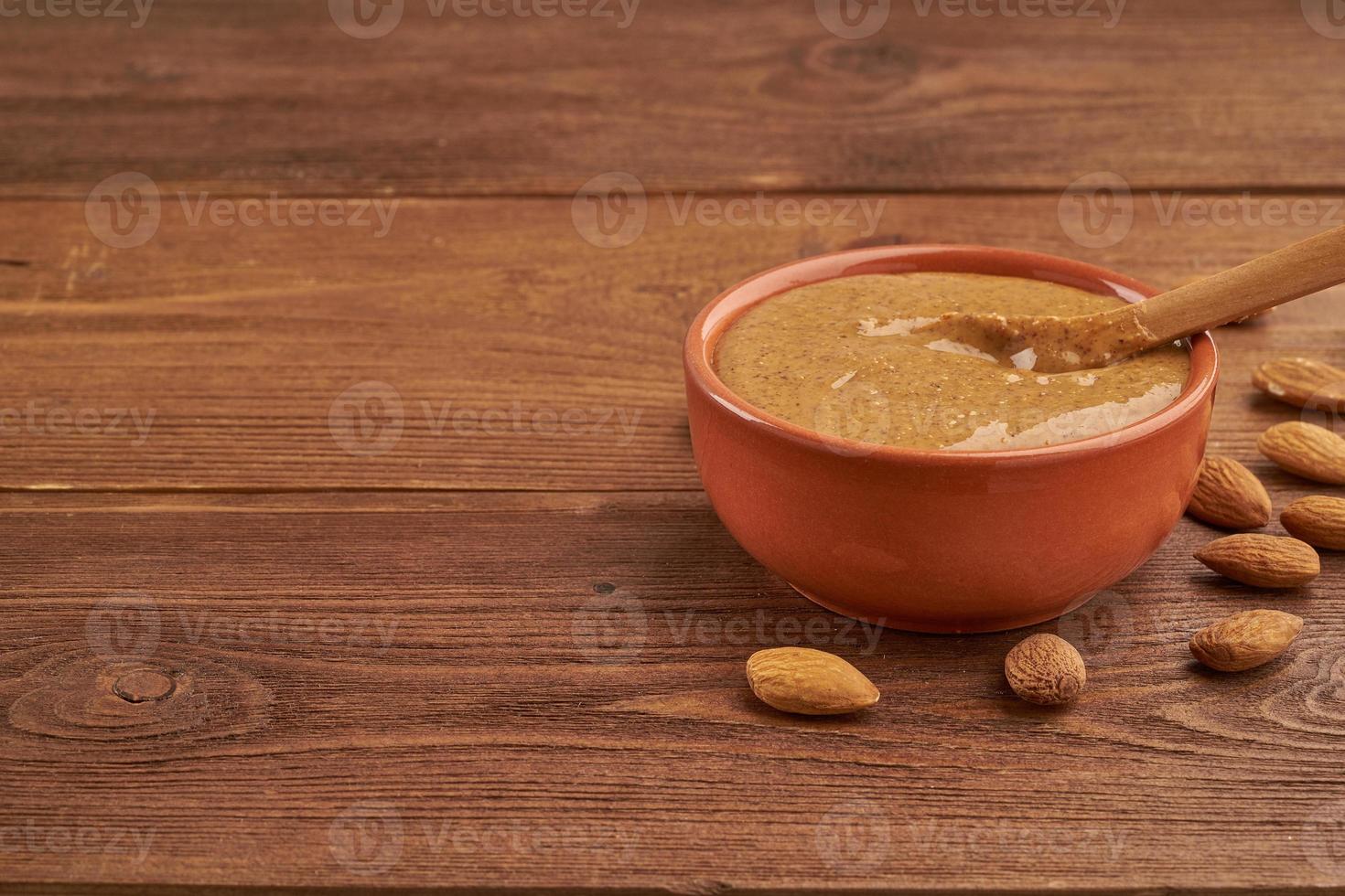 burro di mandorle, pasta alimentare cruda a base di mandorle tritate in un burro di noci, croccante e mescolato, tavolo in legno marrone scuro, spazio per la copia, vista laterale foto