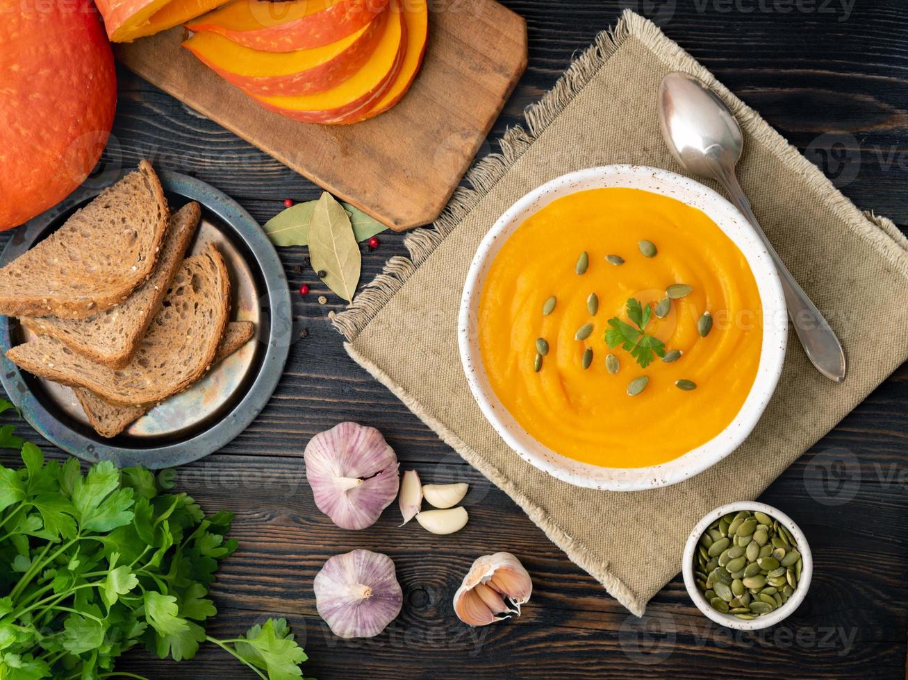 zuppa di zucca schiacciata in un piatto bianco, semi di zucca, pane, aglio su fondo di legno scuro foto