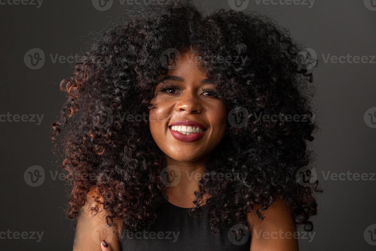 giovane donna afro-americana con i capelli ricci che guarda l'obbiettivo e sorridente. carina ragazza afro con i capelli ricci che sorride guardando la fotocamera. foto