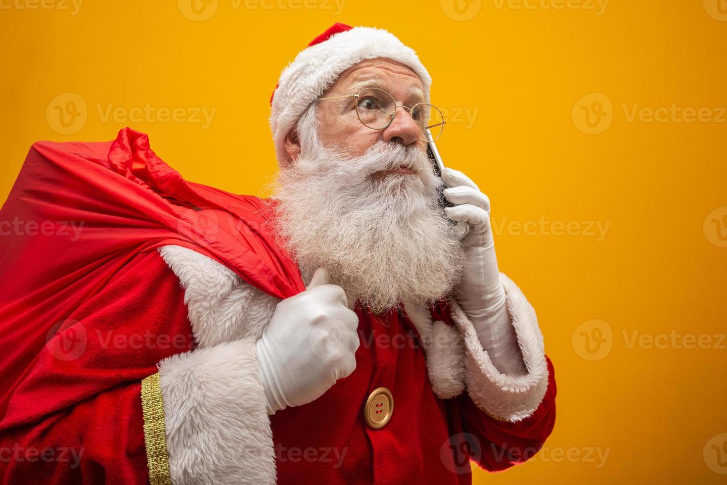 holly jolly x mas santa in copricapo, costume, cintura nera, guanti bianchi porta regali per bambini, preparati per festeggiare, promozione saldi, inverno dicembre, chiacchierando al telefono. Babbo Natale che parla al telefono foto