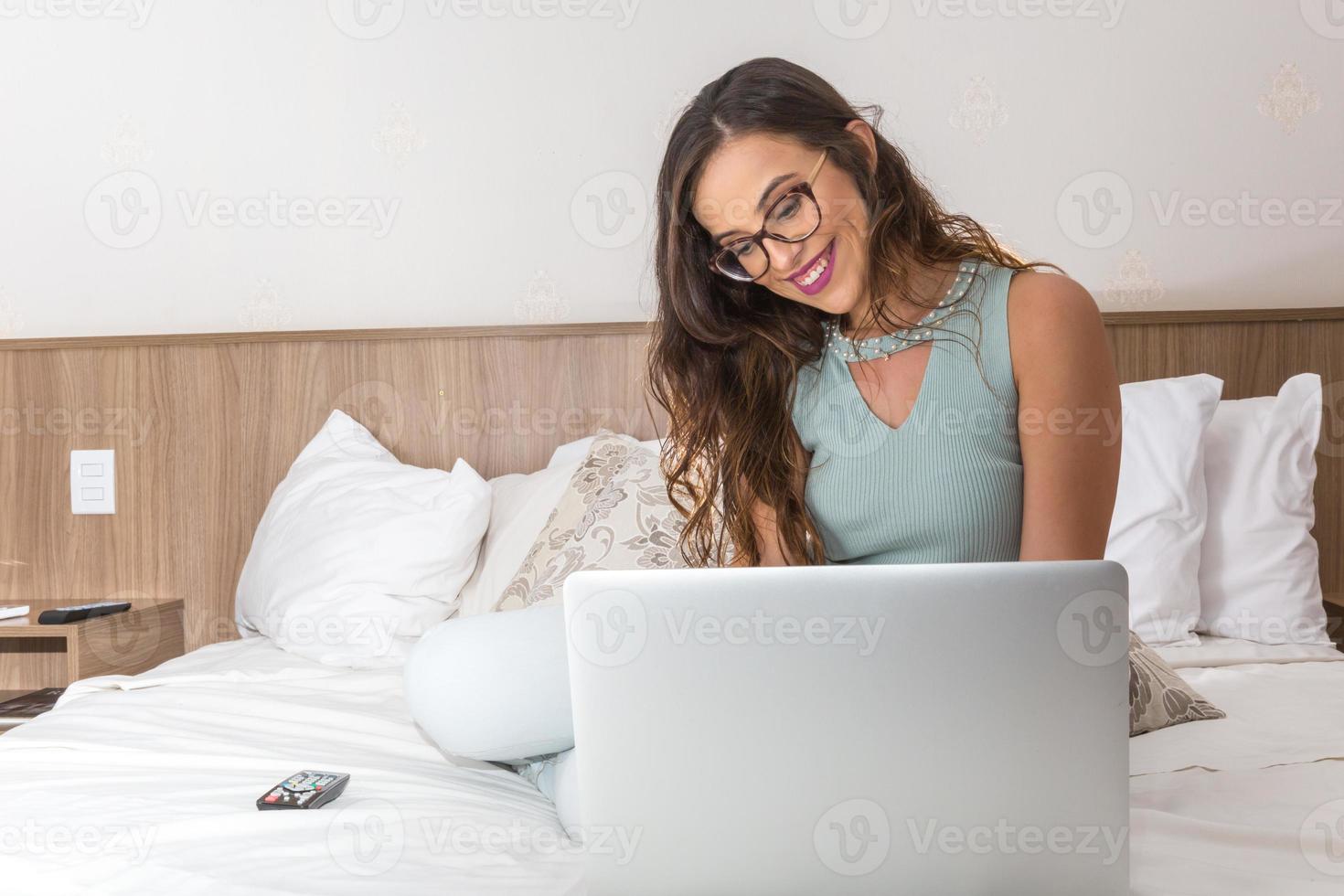 felice casual bella donna che lavora su un computer portatile seduto sul letto in casa. foto