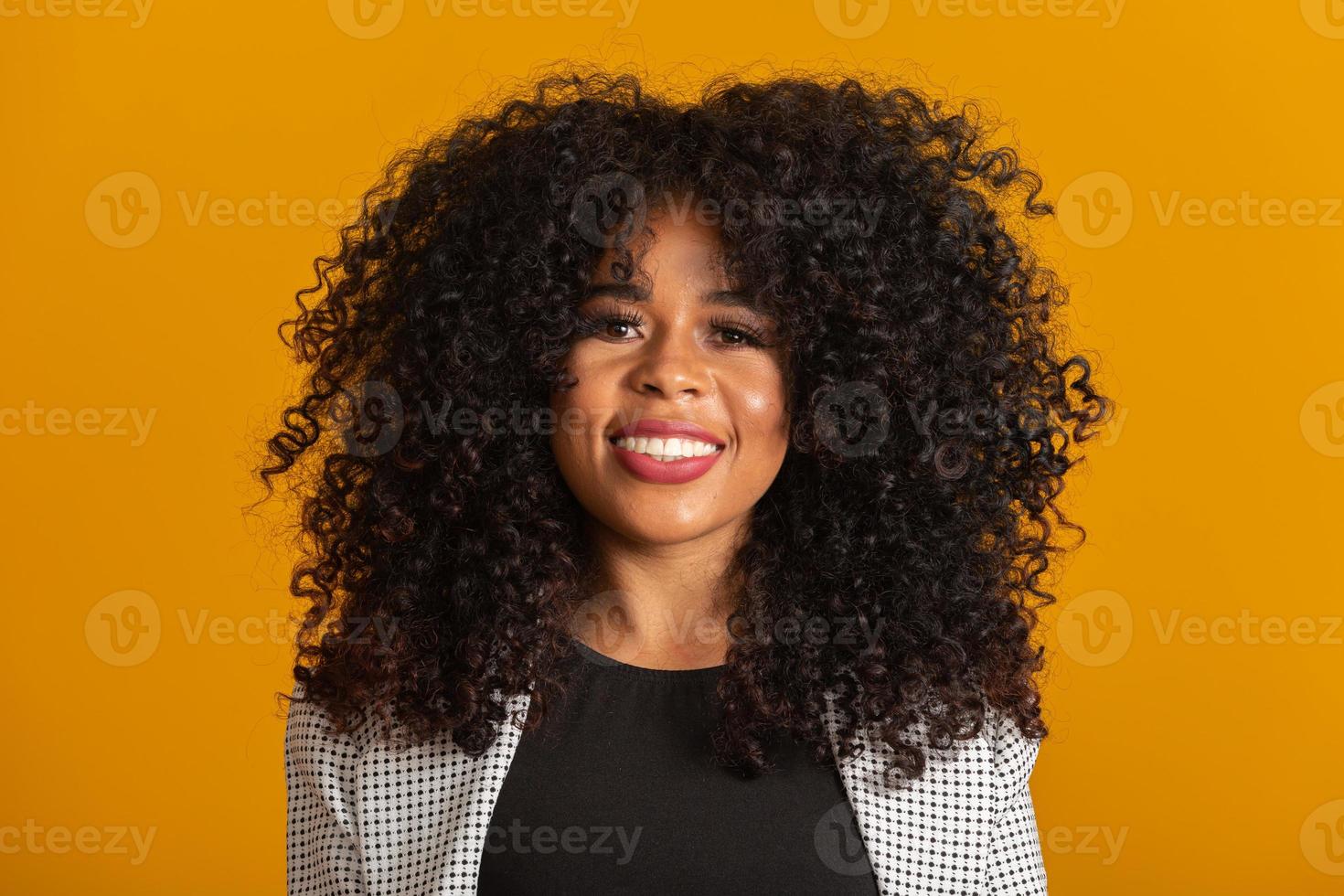 giovane donna afro-americana con i capelli ricci che guarda l'obbiettivo e sorridente. carina ragazza afro con i capelli ricci che sorride guardando la fotocamera. foto