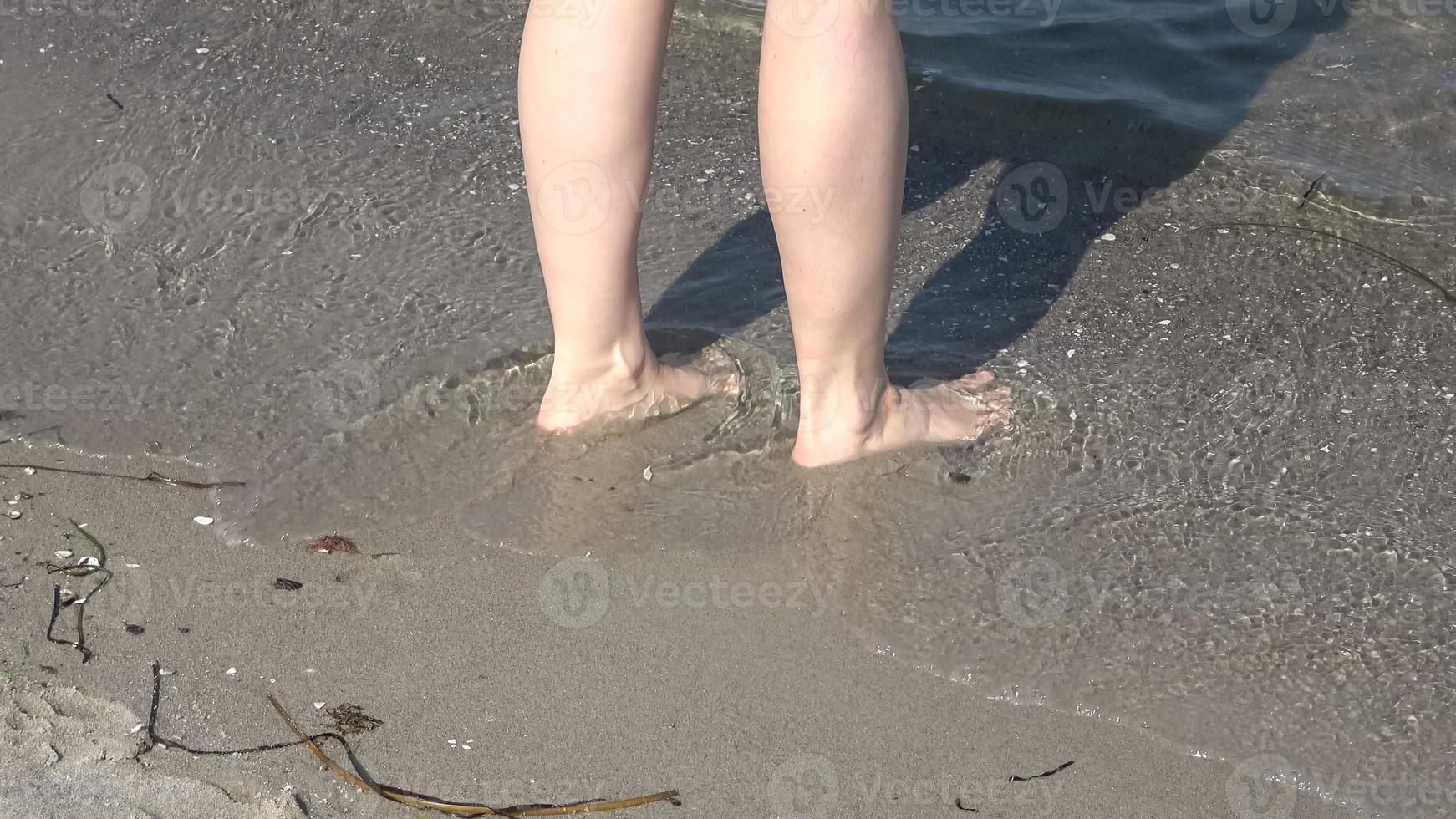 giovani piedi femminili che camminano in acque poco profonde su una spiaggia del Mar Baltico in estate foto