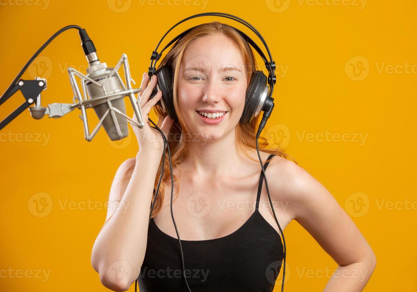 bella donna rossa faccia cantando con un microfono d'argento a condensatore bocca aperta eseguendo la canzone posa su sfondo giallo copia spazio per il testo. annunciatore radiofonico fm. foto